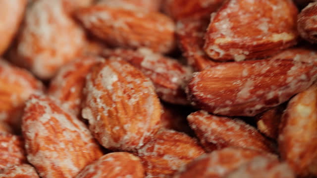 Fried almond in sugar, production of sugared nuts. Factory of healthy sweet food. Cooking dessert snack close-up.