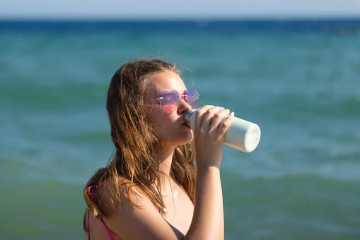 Close up of young woman in swimsuit drinking water from reusable  bottle