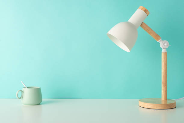 istock Enhance study efficiency with this side-view snapshot of a student's workplace, featuring white table with desk lamp and cup on pastel teal isolated background, perfect for text or advert inclusion 1599301581
