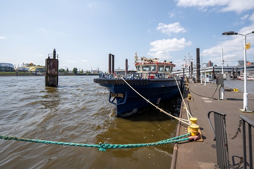 Hamburg, Germany – May 27, 2023: A small vessel bobbing in the water near a dock, with a picturesque landscape in the background