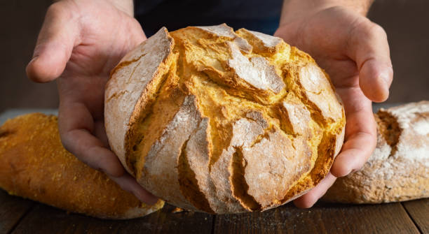 istock Male baker hands holding fresh loaf of bread 1599321457