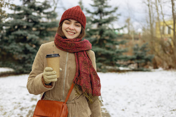 istock Smiling woman with coffee cup in winter park 1599386178