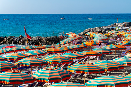 Lone striped umbrella leaning into wind on a sandy French beach in summer with a blue clear sky background