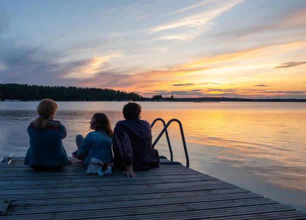 Women, an elderly woman, a young woman and a girl of 8 years old, a Caucasian family spend time together, look at the beautiful sunset and enjoy the scenery. On the lake on a wooden pier. Caucasian family watching sunset at Saimaa Lake in South Korea Finland. An elderly woman 77 years old, a woman 40 years old and a girl 8 years old. saimaa stock pictures, royalty-free photos & images