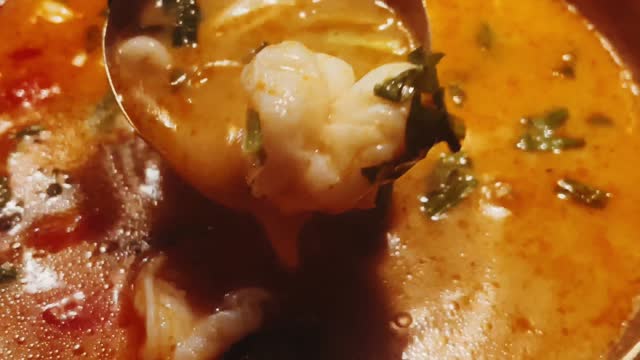 Close-up of a spoon dipping into a rich and flavourful seafood soup, made with a spicy tomato broth and loaded with fresh fish and shellfish