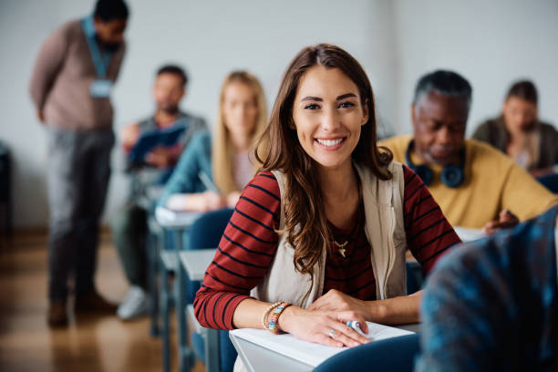 Happy female student learning in the classroom and looking at camera. Young happy woman attending adult education training class in lecture hall and looking at camera. post secondary education stock pictures, royalty-free photos & images
