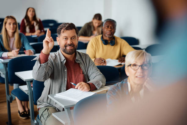 istock Mature man raising hand to ask a question while attending a class in lecture hall. 1599476332