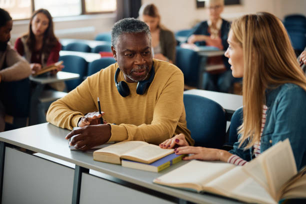 istock Black senior man communicating with female classmate during educational training class in lecture hall. 1599476874