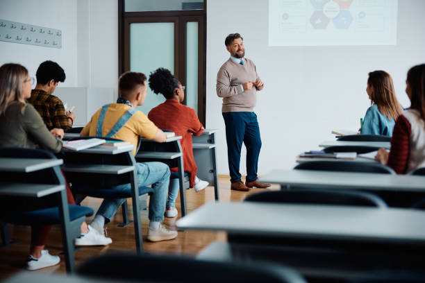 Happy university professor giving a presentation to group of students in lecture hall. Happy teacher talking while giving a lecture to university students in the classroom. projector screen classroom stock pictures, royalty-free photos & images