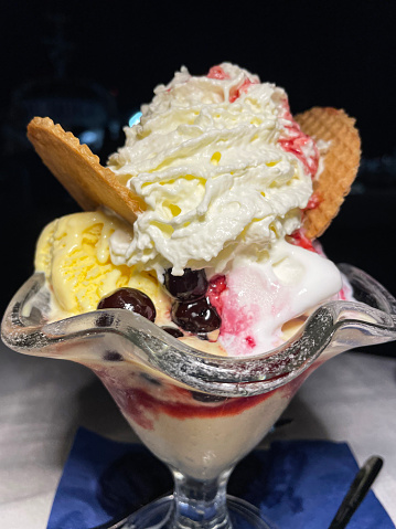 Stock photo showing close-up view of restaurant dessert of scoops of vanilla and cherry gelato served with wafers and spray cream in a white dish.