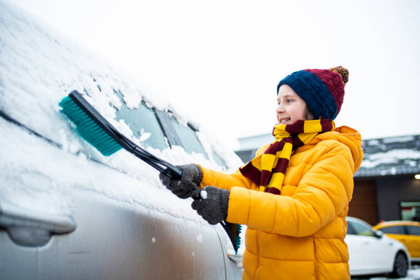 愛らしい男の子は、両親が車のフロントガラスから雪を取り除くのを手伝います。笑顔の幸せな小さな子供が冬に車の窓から雪を掃除します。 - snow car window ice scraper ストックフォトと画像