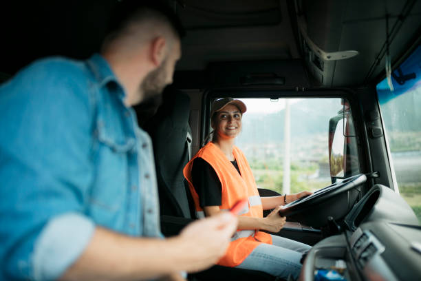 Woman driver driving a truck and talking with delivery worker sitting on passenger seat stock photo