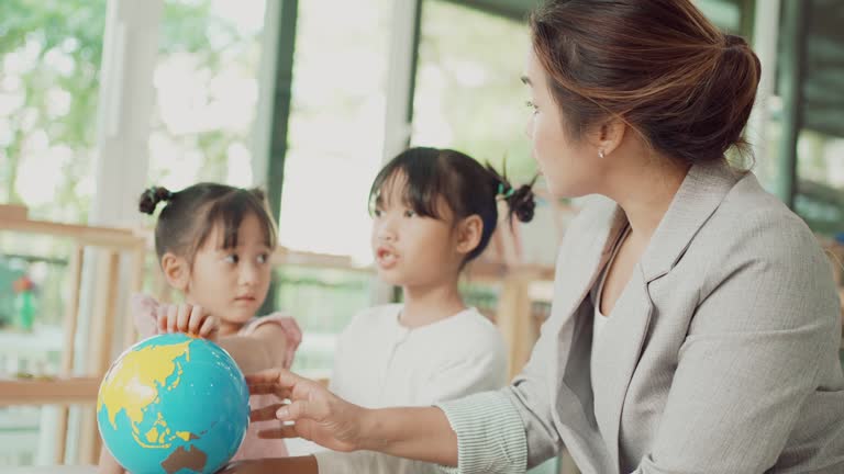 Elementary and preschool girls learning world map with model globe with teacher in Montessori education school