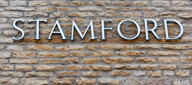 The single word Stamford, in individual metal and vitreous enamel capital letters, offset against the archetypal building material for the town, Jurassic Lincolnshire Limestone. The town has many historic 17th and 18th century stone buildings and many older timber-framed buildings and five medieval parish churches. Largely unspoilt by modern building developments, Stamford is frequently chosen as a film location