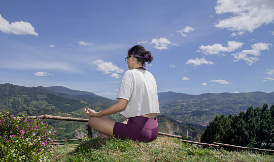 Young woman practicing yoga outdoors, among the mountains on a sunny day