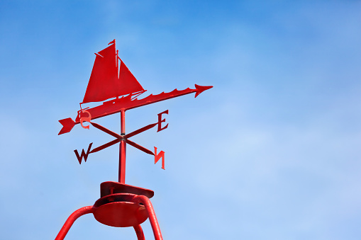 Red painted Sailboat Weather Vane against a blue sky, at Morston Quay, near Blakeney, on the North Norfolk Coastline in the Norfolk Area of National Beauty (AONB), a popular are for leisure boat recreational pursuits. Good copy space.