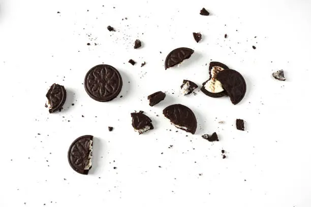 Top view of broken sandvish chocolade cookies with milky cream on white background.