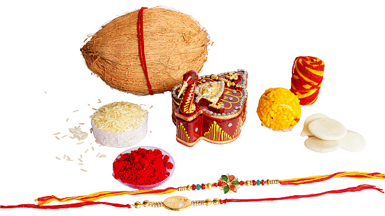 Raksha Bandhan festival Concept showing designer Rakhi or Wrist Band with Gifts, Sweets and coconut arranged over white background.