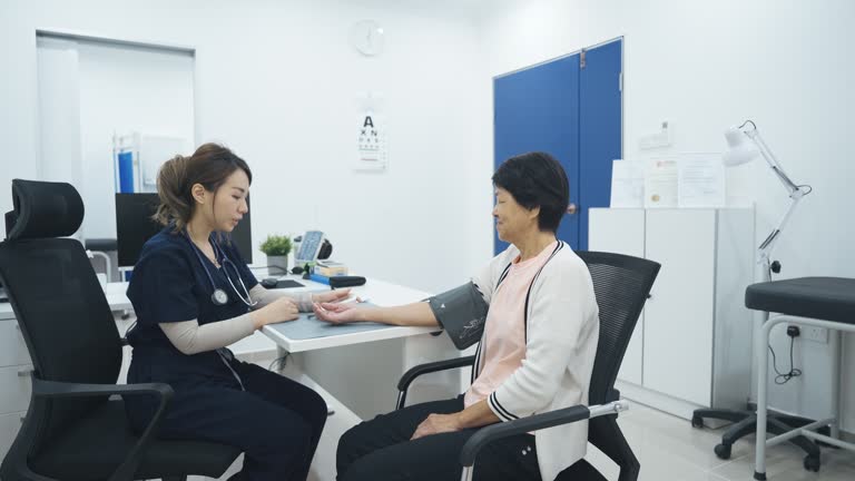 Asian chinese doctor measuring senior woman's blood pressure in clinic