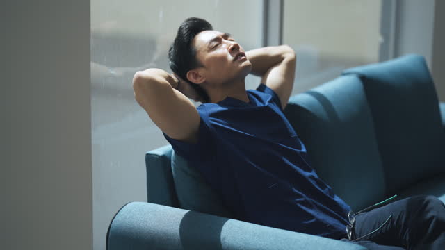 exhausted Asian Chinese male nurse resting on sofa taking a break