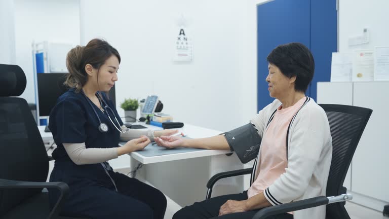 Asian chinese doctor measuring senior woman's blood pressure in clinic