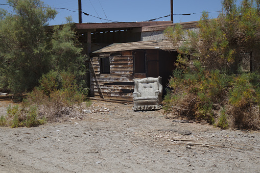 Abandoned vintage white couch in front of a derelict wood cabin in the desert in Salton Sea.