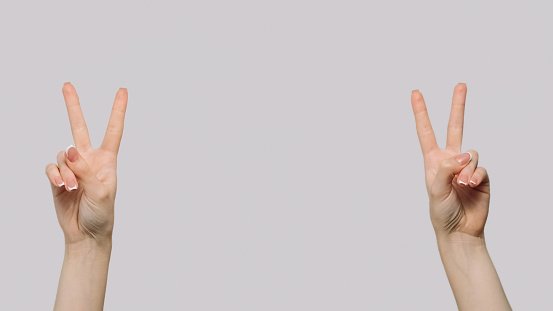 Victory sign. Peace gesture. Female hands showing v symbols demonstrating winning with fingers isolated on gray copy space background.