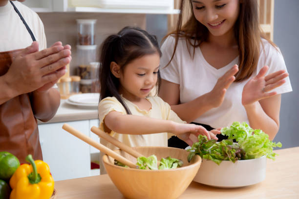 Happiness asian family with father, mother and daughter preparing cooking salad vegetable food together in kitchen at home, happy dad, mom and kid cooking breakfast with salad, lifestyles concept. stock photo