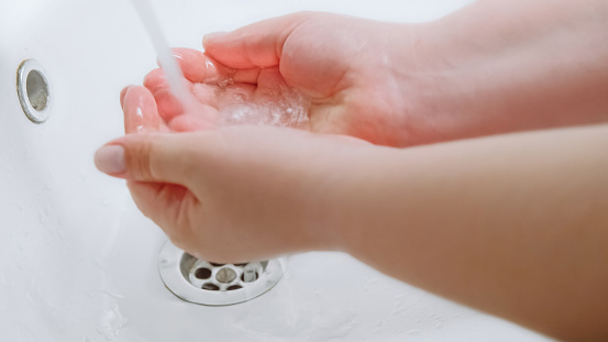 Clean hands. Bacteria prevention. Virus hygiene. Woman washing palms skin with water to protect from microbes infection spreading in white sink.