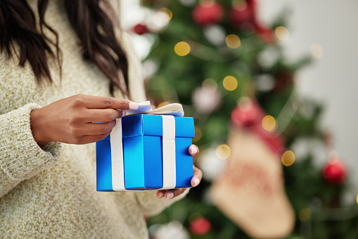 Closeup, hands and woman with a gift, Christmas and box with a package, living room and celebration. Zoom, female person or girl with a Xmas present, festive season and product with holiday and party
