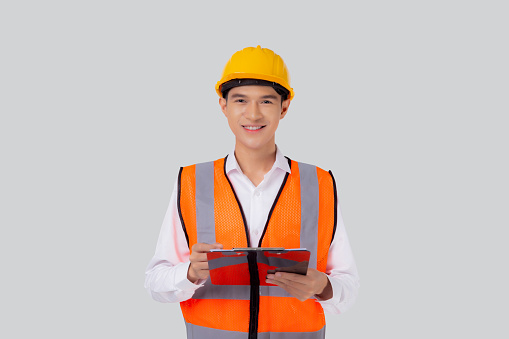 Portrait young asian engineer man wearing helmet looking document or report on clipboard isolated white background, architect or contractor check and diagnostic for planning, industrial concept.