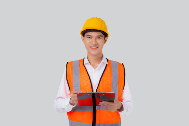 Portrait young asian engineer man wearing helmet looking document or report on clipboard isolated white background, architect or contractor check and diagnostic for planning, industrial concept. stock photo