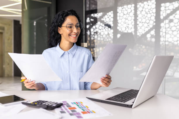 istock latin american businesswoman working inside office with documents and laptop, worker paperwork calculates financial indicators smiling and happy with success and results of achievement and work 1599879743