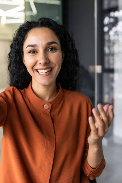istock Vertical shot, video call from office hispanic business woman working inside modern office building, talking remotely with friends using app on phone for video call. 1599879787