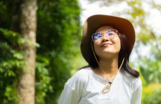Glasses Asian girl smiling and stares at the sky to explore the mountains, the sunshine, to set the direction of a holiday trip. Portrait, copy space, travel concept.
