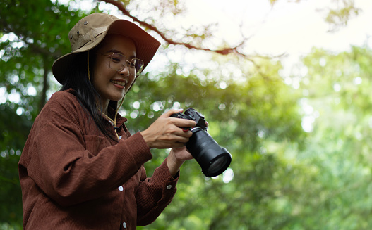 Shot of happy photographer women holding a camera and checking her picture in nature on her forest trip. Close up, copy space.