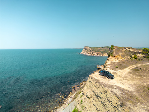 Offroad car with a roof top tent camping on the cliff edge by the adriatic sea in Albania. Aerial view at sunset.