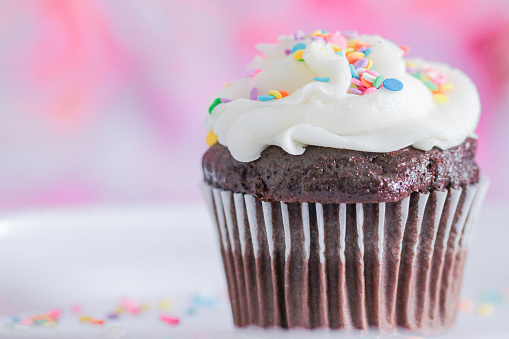 Chocolate cupcake with white vanilla icing on pink background with sprinkles