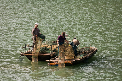 Vietnam, Asia- August 20,2023:A small fishing boat motoring in a calm sea in Halong Bay with misty limestone karsts behind Vietnam