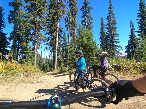 Personal perspective of a senior Chinese woman and her multiracial adult daughter mountain biking preparing to enter a downhill mountain biking trail through a forest in British Columbia, Canada.  Taken on a wearable camera.