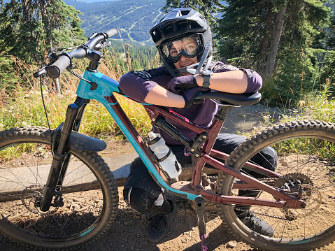 Eurasian young woman resting before going downhill mountain biking through an alpine forest in British Columbia, Canada.