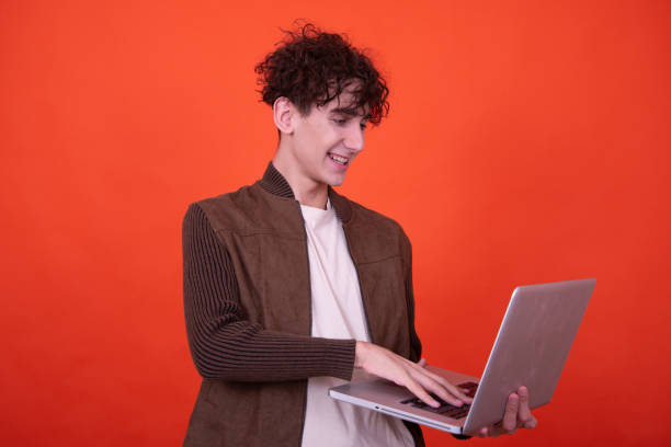 istock Funny guy with a laptop posing on an orange background. 1600188043