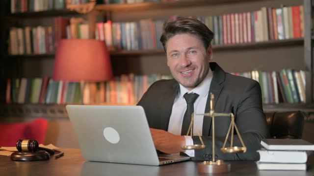 Smiling Male Lawyer Looking at Camera while Working on Laptop