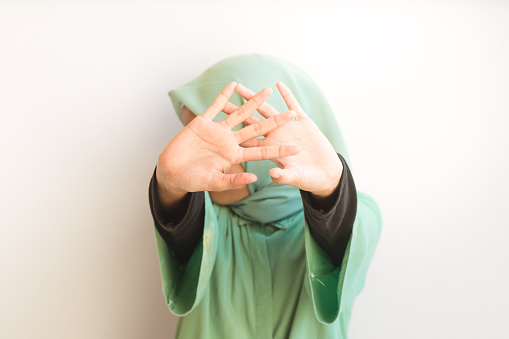 Portrait of an Asian Muslim young girl open palm to the camera, covering his face. Stop gesture