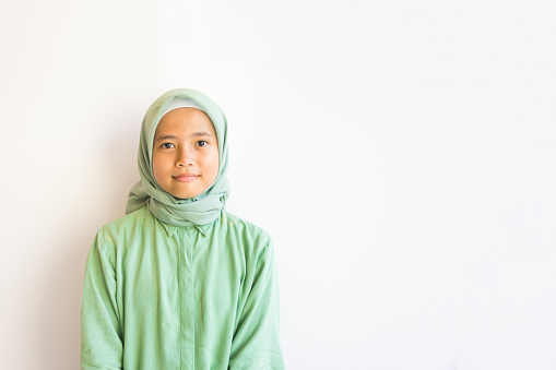 Medium shot of an Asian Muslim girl smiling while looking at the camera on white background, she's wearing a casual outfit, innocent and pure, with copy space
