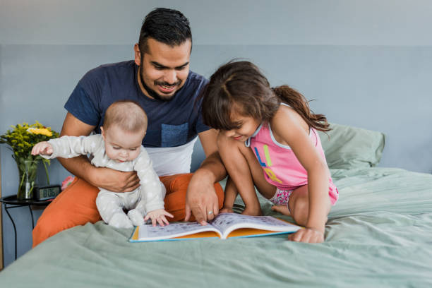 young latin family with children reading a book together on bed at home in Mexico, Hispanic mother, father, daughter and baby in Latin America young latin family with children reading a book together on bed at home in Mexico, Hispanic mother, father, daughter and baby in Latin America 6 9 months stock pictures, royalty-free photos & images