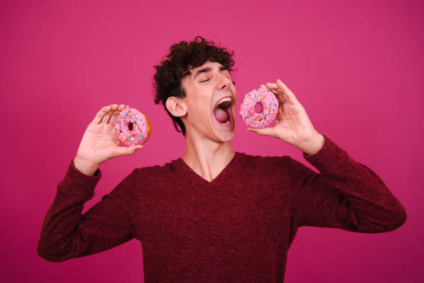 istock Young attractive guy eats pink donuts. Delicious breakfast and good vibes. 1600317389