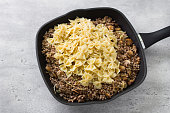 Traditional jewish dish kasha varnishkes: buckwheat, champignon mushrooms, fried onions, farfalle pasta in frying pan on gray textured background, cooking homemade food, top view