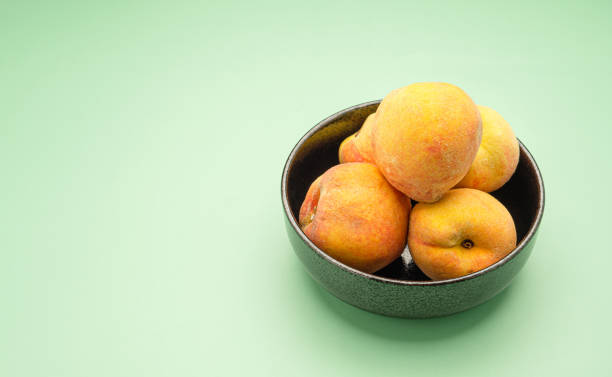 緑の背景に新鮮な桃の実をボウルに - fruit vegetable fruit bowl peaches ストックフォトと画像