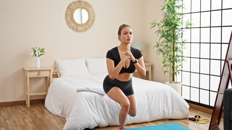 Young beautiful hispanic woman wearing sportswear doing legs exercise at bedroom